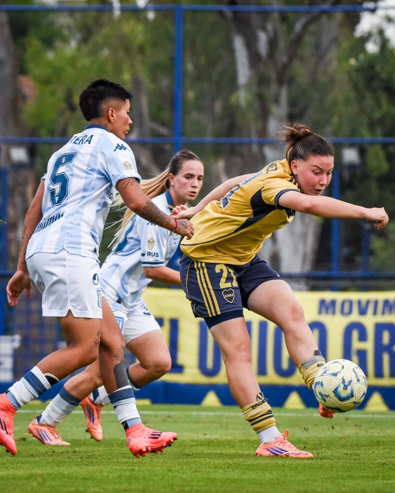 Julieta Martínez pasa la pelota mientras Gabriela Herrera la presiona. De fondo, Agostina Holzheier está atenta a la acción.